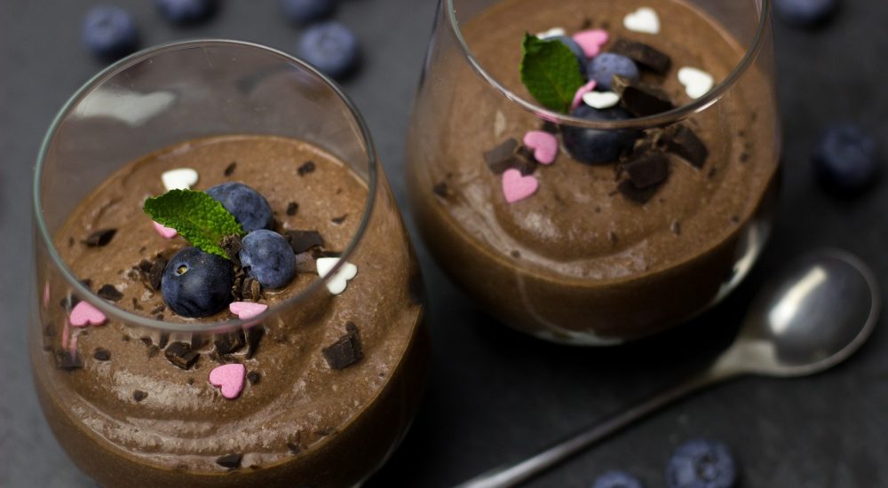 Bild: 2 Gläser mit vollwertigem Schokoladen Glace dekoriert mit chocolate chips und Heidelbeeren auf schwarzem Tisch.